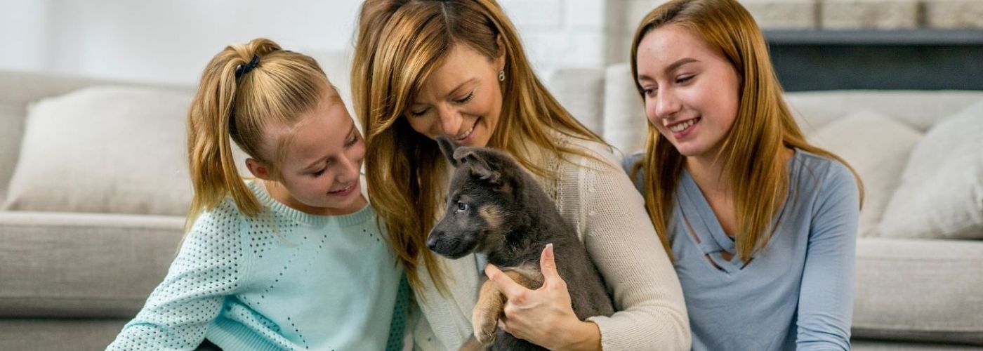 A woman and two young people smiling at a small German Shepherd puppy held by the woman.